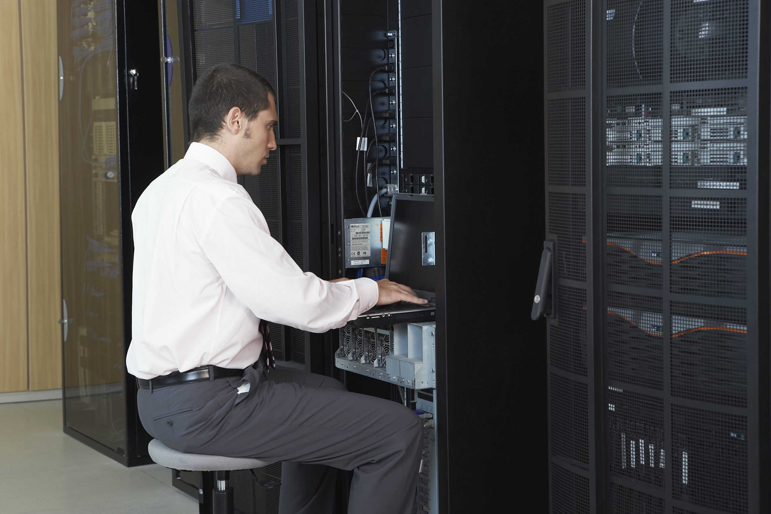 A person is sat infront of a metal rack of servers within a datacenter.